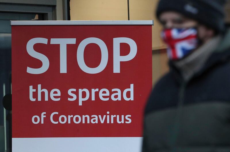 A man wearing a British union flag face mask walks past a coronavirus advice sign outside a bank in Glasgow the morning after stricter lockdown measures came into force for Scotland, Tuesday Jan. 5, 2021.  Further measures were put in place Tuesday as part of lockdown restrictions in a bid to halt the spread of the coronavirus.(Andrew Milligan/PA via AP)