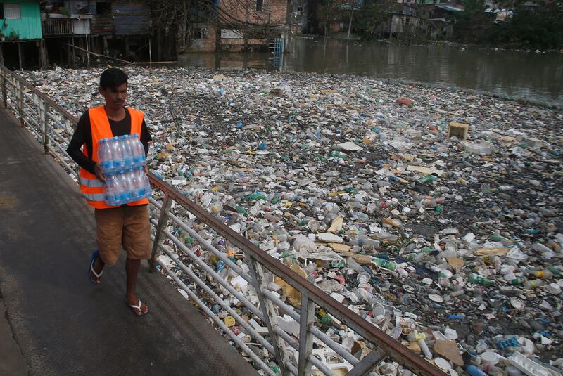A man carries water bottles across the heavily polluted Negro River in Manaus, Brazil. About 35 tonnes of rubbish are removed daily from the river. AP