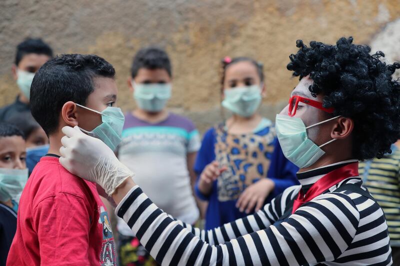 Egyptian clown Ahmed Naser helps children to put on face masks as a preventive measure against the spread of the coronavirus disease, in Darb Al-Ban district in Cairo, Egypt.  EPA