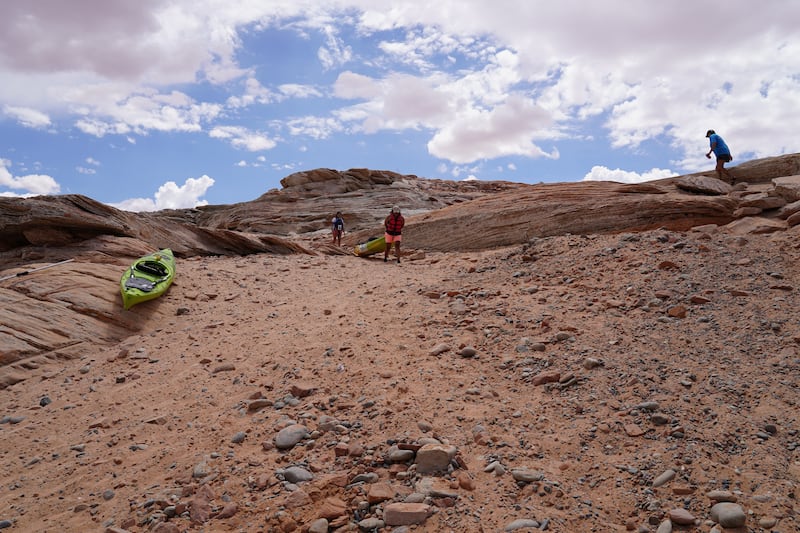 Kayakers carry their boats down the rocky banks of Lake Powell. In normal years, they would be able to float their kayaks off the tarmac ramp.