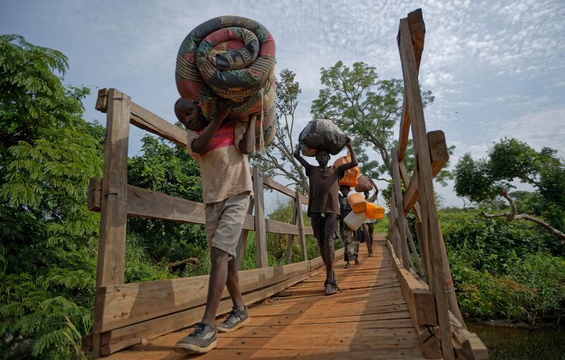 FILE - In this Thursday, June 8, 2017 file photo, from left to right, South Sudanese refugees Thomas Wani, 12, brother Peter Lemi, 14, mother Rose Sunday, and father Julius Lezu, cross a wooden bridge from South Sudan to Uganda at the Busia crossing, near Kuluba, in northern Uganda. The number of South Sudanese refugees sheltering in Uganda has reached 1 million, the United Nations said Thursday, Aug. 17, 2017, a grim milestone in what has become the world's fastest-growing refugee crisis. (AP Photo/Ben Curtis, File)