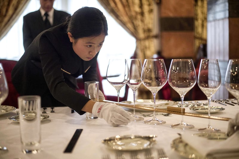 A butler in training inspects the cutlery on a table.