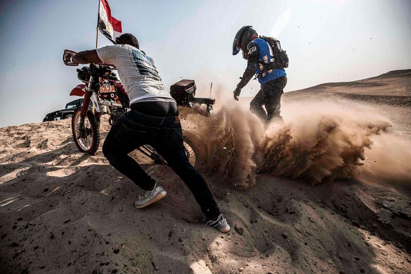 An assistant helps a rider get his stuck motorcycle out of the sand during the 'Egypt Motorcycle Rally' near the Abusir pyramids in the desert between Giza and Saqqara, about 35km south of Egypt's capital Cairo.  AFP