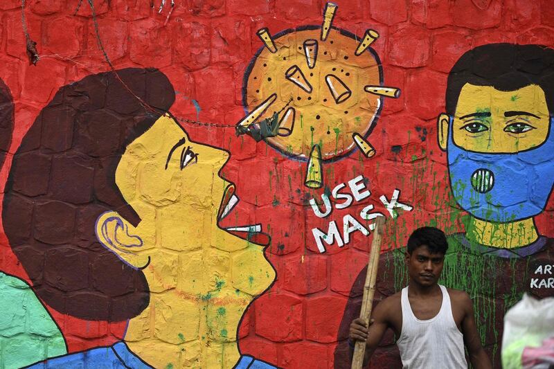 A ragpicker stands in front of a mural on COVID-19 coronavirus awareness, painted on a wall along the roadside in New Delhi on July 23, 2020. India last week became the third country after the United States and Brazil to hit one million cases but many experts say that with testing rates low, the true number could be much higher. / AFP / SAJJAD  HUSSAIN
