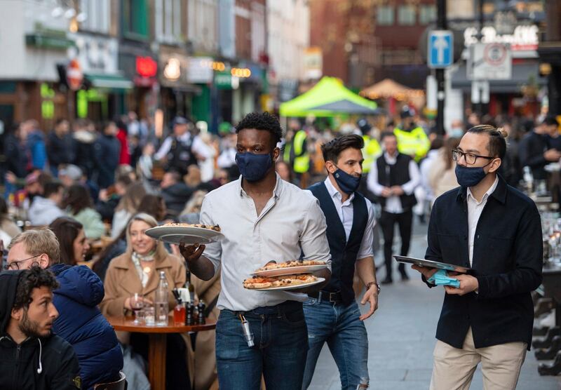 Waiters serve people eating and drinking at outside tables on Saturday evening, April 24, 2021, in Soho, central London, following the further easing of lockdown coronavirus restrictions in England. (Dominic Lipinski/PA via AP)