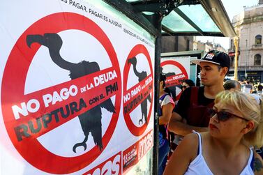 Pedestrians walk past posters on a Buenos Aires street urging Argentina to default on its debt and break with the IMF. Reuters