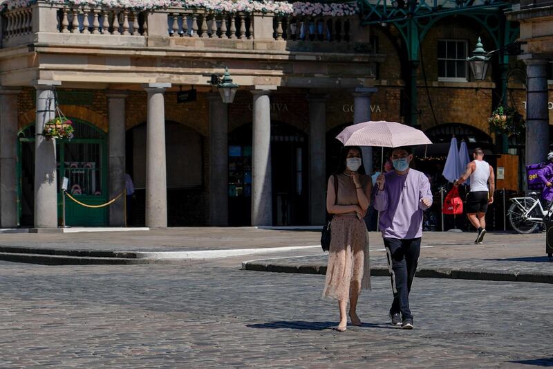 A couple wear face masks as they shelter from the sun under an umbrella, while they walk in Covent Garden, in London. AP Photo