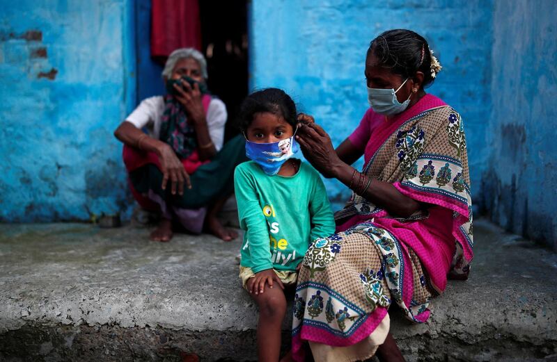 A woman wearing a protective face mask adjusts her daughter's face mask outside their house in a slum area. Reuters