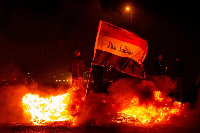 A protester holds a national flag as he stands by a fire in Basra. AFP
