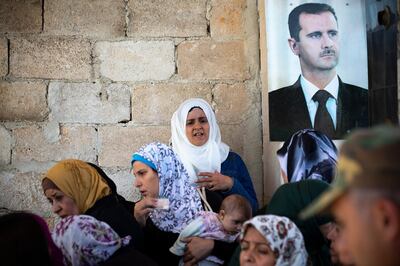 People who returned to Khan Sheikhoun after it was captured by government forces lineup to to check their documents with a portrait of Syrian President Bashar Assad at right, in the Syrian town of Khan Sheikhoun, Syria, Wednesday, Sept. 25, 2019. The town, which holds a strategic position in Syria's northwestern Idlib province, fell to Assad's forces last month following weeks of a massive offensive by Syrian troops backed by Russian military support. (AP Photo/Alexander Zemlianichenko)