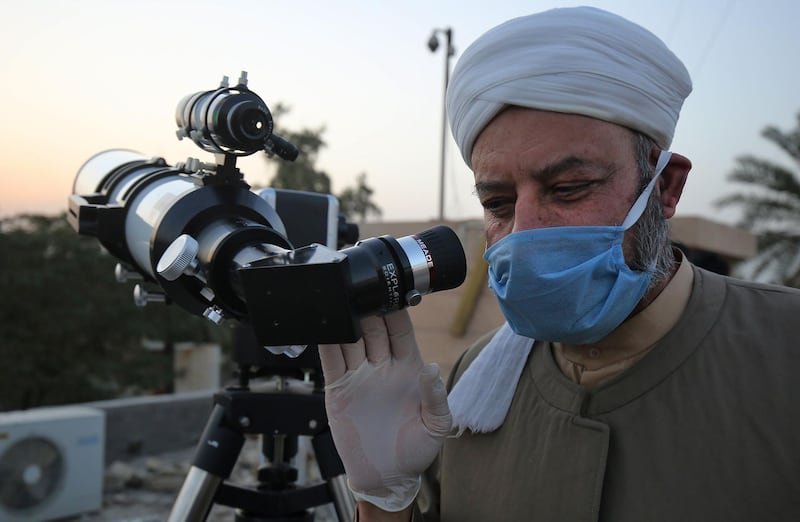 A Sunni Muslim cleric wearing a face mask uses a telescope to gaze while searching for the crescent moon, which if sighted would mark the beginning of the Muslim holy month of Ramadan, at the Abu Al Hanifa Al Numan mosque in the Adhamiya district of Iraq's capital Baghdad.  AFP