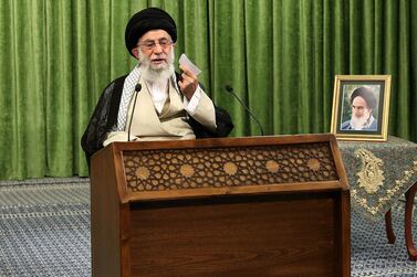 Iran's supreme leader Ayatollah Ali Khamenei sits beside a photo of his predecessor, the late ayatollah Ruhollah Khomeini, during an online meeting. khamenei.ir / AFP