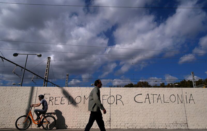 People pass in front of graffiti reading "Freedom for Catalonia" in Barcelona, Spain, Monday, Oct. 23, 2017. Catalonia's regional parliament will hold a debate this week on Spain's plan to take direct control of the northeastern region �������� a session many fear could become a cover for a vote on declaring independence. (AP Photo/Manu Fernandez)