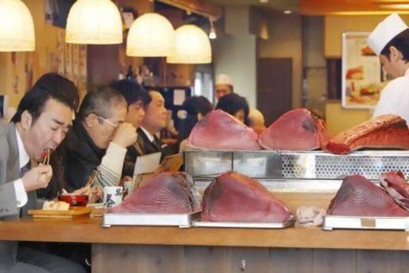 People eat sushi alongside blocks of tuna in Tokyo. The Fukushima nuclear disaster left the Japanese fishing industry reeling. Koji Sasahara / AP Photo