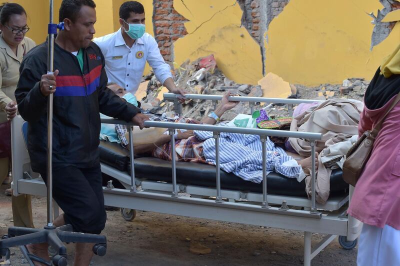 An injured quake victim is wheeled past a damaged wall in Mataram on the Indonesian island of Lombok. AFP