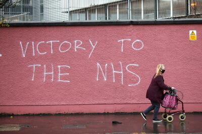 A woman walks past graffiti with the words Victory to the NHS (National Health Service) on a wall at the Royal Victoria Hospital, one of several hospitals around Britain that are handling the initial phase of a COVID-19 immunization program, in West Belfast, Northern Ireland, Tuesday, Dec. 8, 2020. British health authorities rolled out the first doses of a widely tested and independently reviewed COVID-19 vaccine Tuesday, starting a global immunization program that is expected to gain momentum as more serums win approval. (AP Photo/Peter Morrison)