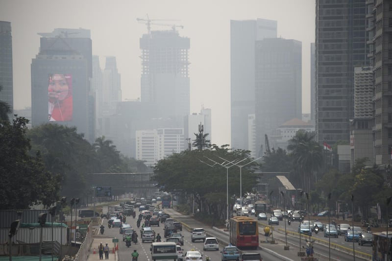 This photograph taken on August 8, 2018 shows a 2018 Asian Games promotional billboard on a building (L) as seen past traffic and haze from air pollution in Jakarta's city centre. - Indonesia is about to open the Asian Games but its traffic-clogged capital Jakarta remains shrouded in a haze of air pollution that threatens to mar the world's second-biggest multi-sport event. (Photo by BAY ISMOYO / AFP)