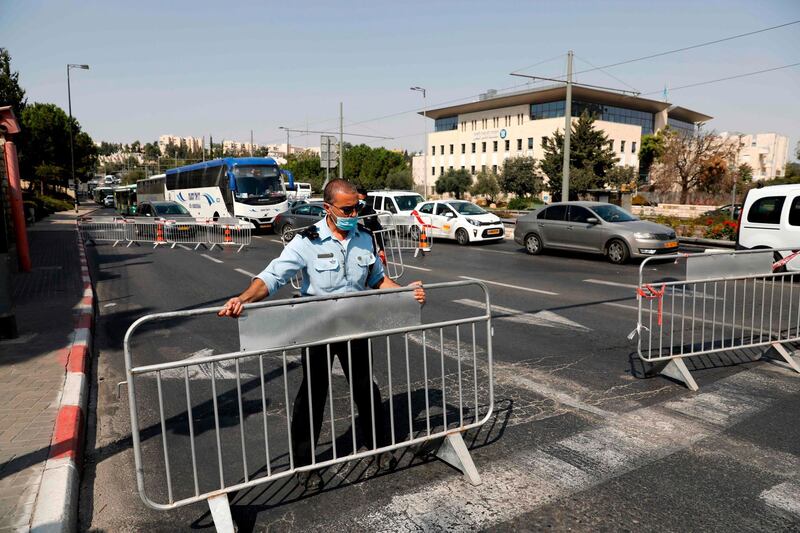 Members of the Israeli police set up barriers to traffic at a checkpoint in Jerusalem on September 18, 2020, to enforce a second lockdown amid the COVID-19 pandemic. Israel imposed a second nationwide lockdown to tackle one of the world's highest coronavirus infection rates, despite public protests over the new blow to the economy. The three-week shutdown from 2:00 pm (1100 GMT) started just hours before Rosh Hashana, the Jewish new year, and will extend through other key religious holidays, including Yom Kippur and Sukkot. / AFP / Ahmad GHARABLI
