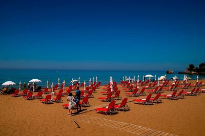 People stand next to sunbeds on the Glyfada beach in the island of Corfu on June 30, 2020 as the island welcomes its first tourists after months of closure due to the spread of the Covid-19 disease caused by the novel coronavirus.   Greece on July 1, 2020 reopened flights to its flagship island destinations as it raced to salvage a portion of the annual tourism season that is vital to its economy. / AFP / ANGELOS TZORTZINIS
