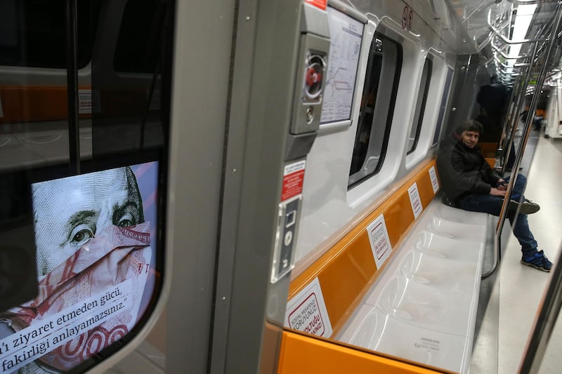 Commuters in an underground train are driven past a billboard of a book advertisement featuring a picture of U.S. President Benjamin Franklin on the 100-U.S. dollar bill, in central Istanbul, Friday, April 3, 2020. The new coronavirus causes mild or moderate symptoms for most people, but for some, especially older adults and people with existing health problems, it can cause more severe illness or death. (AP Photo/Emrah Gurel)