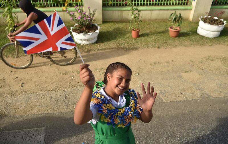 A girl holds a Union Jack flag as she cheers for Britain's Prince Harry and his wife Meghan, Duchess of Sussex as their convoy from Fua'amotu airport in Tonga passes by. Prince Harry and his pregnant wife Meghan left Fiji after a three-day official visit and arrived in Tonga as part of their tour of Australia and the South Pacific. AFP