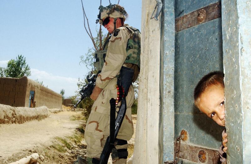 HESARAK, AFGHANISTAN - JULY 16:  An Afghan child peeks out from the doorway of his family's home as US Army soldier from the 101st Airborne stands guard in the eastern Afghan village of Hesarak on July 16, 2002 during what the Army refers to as a 'sensitive site exploitation' mission or 'SSE'. The army says that Hesarak was raided for the first time four days ago when undisclosed intelligence materials were gathered.  Today's raid was intended both to search for more materials and to provide some hunanitarian aid to local residents.   (Photo by Scott Nelson/Getty Images)