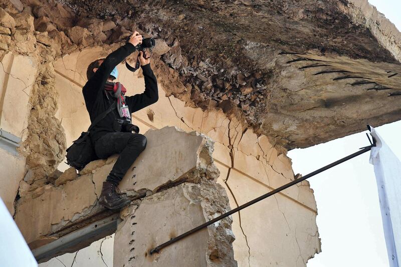 A photojournalist uses his camera from atop a broken wall near the ruins of the Syriac Catholic Church of the Immaculate Conception (al-Tahira-l-Kubra), in the northern city of Mosul, amidst preparations ahead of the Pope's visit, on March 7, 2021.  Pope Francis, on his historic Iraq tour, visits today Christian communities that endured the brutality of the Islamic State group until the jihadists' "caliphate" was defeated three years ago / AFP / Vincenzo PINTO             
