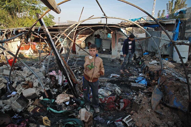 TOPSHOT - A Syrian boy holds a rose inside a charred tent following Syrian regime bombardment on a makeshift camp in the village of Qah near the Turkish border in the northwestern Idlib province on November 21, 2019. The Syrian Observatory for Human Rights, in an updated toll, said a ground-to-ground missile fired by regime forces that hit a makeshift camp for the displaced near Qah village close to the border with Turkey killed 15 civilians, including six children, and wounded around 40 others. The missile crashed near a maternity facility in the camp, it said.
 / AFP / Aaref WATAD
