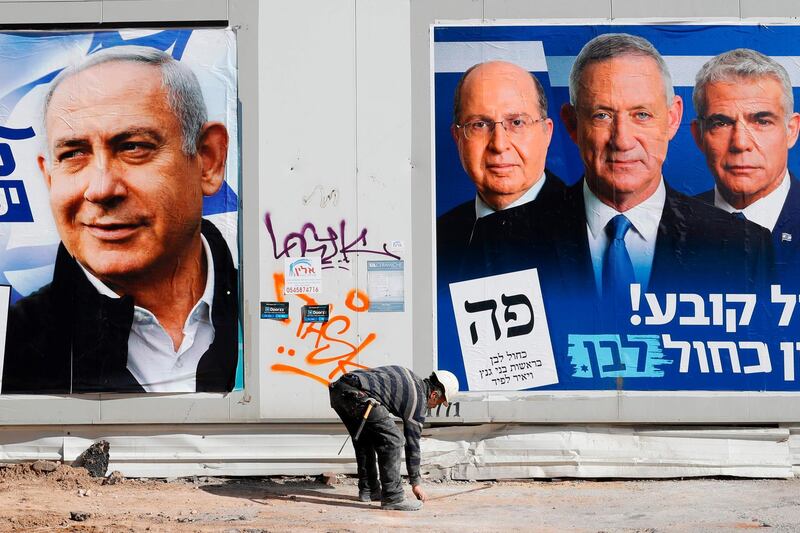 A labourer walks past electoral campaign posters bearing the portraits of Israel's Prime Minister Benjamin Netanyahu (L), leader of the Likud party, and retired Israeli general Benny Gantz (R), one of the leaders of the Blue and White (Kahol Lavan) political alliance, in the Israeli city of Tel Aviv, on April 3, 2019, ahead of the general election scheduled for April 9.  / AFP / JACK GUEZ
