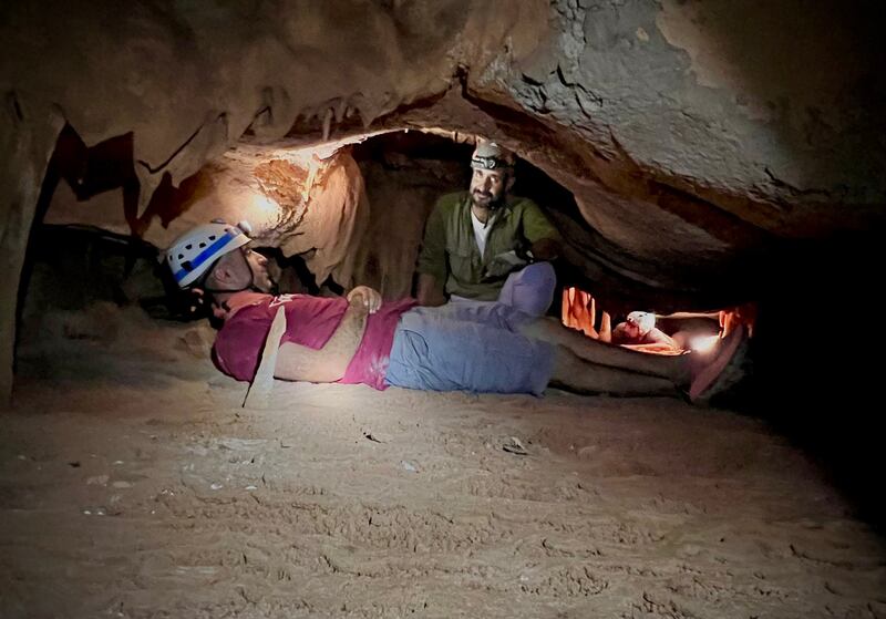 A caver lies on the ground, to manoeuvre in a tight area, during an expedition. Photo: Nabil Alsaqri