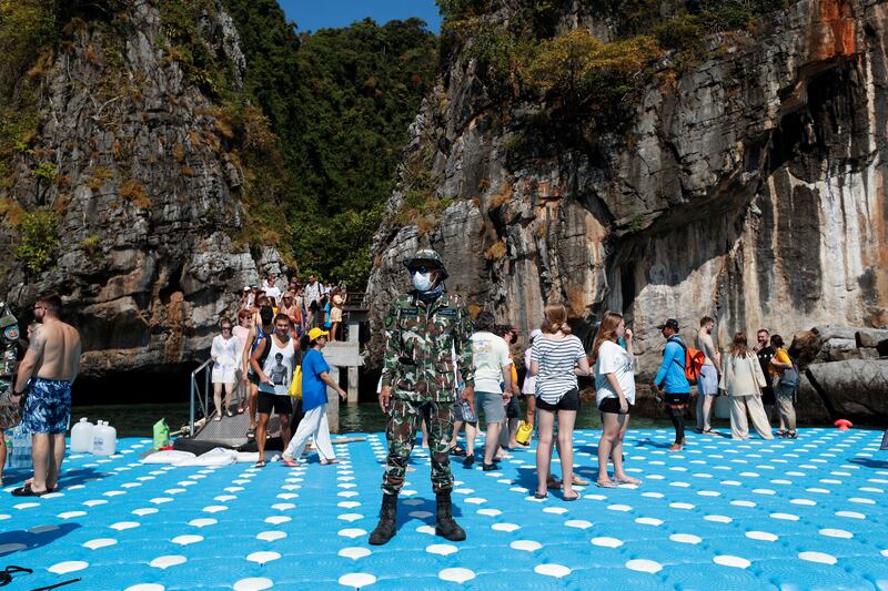 A Thai wildlife department officer wearing a face mask stands guard as tourists visit Maya Bay.