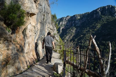 Father Hani Tawk walks along a pathway built along the steep cliff on which the Deir Qannoubine monastery sits. Photo: Finbar Anderson / The National
