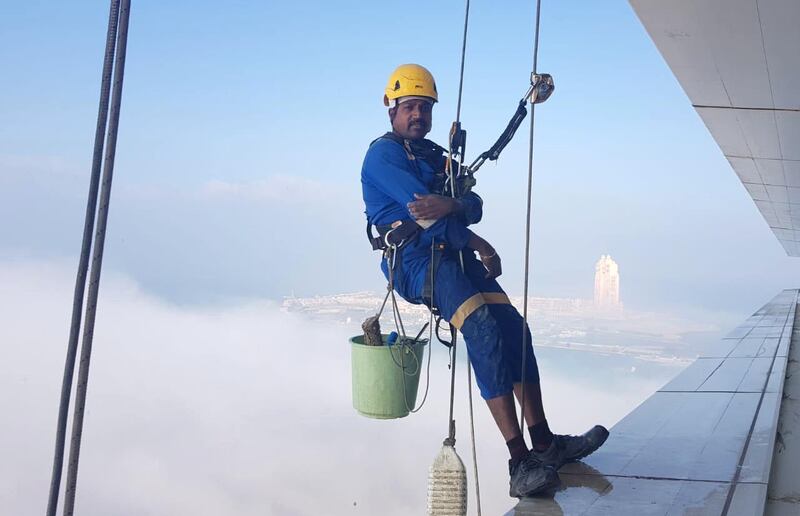 Window cleaners work on Al Ain Tower with view of Etihad Towers in the background in Al Khalidiyah, Abu Dhabi. Erica ElKhershi / The National