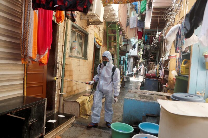 A man wearing personal protective equipment sprays disinfectant on the walls in an alley in a slum area of Mumbai. Reuters