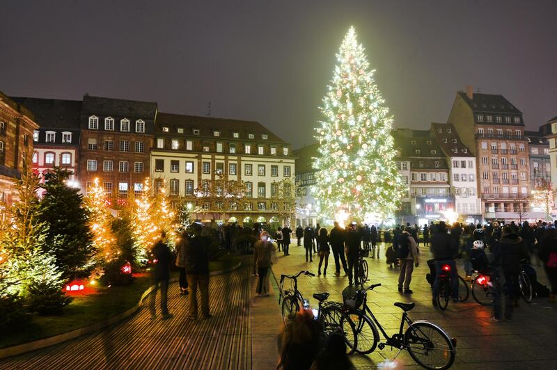 Pedestrians look at the giant Christmas tree on the main square in Strasbourg, eastern France, on November 27, 2020, on the opening day of the city's Christmas Illuminations. - Strasbourg, whose Christmas market is usually one of the most famous, lit up its streets and huge fir tree on November 27, 2020, without the traditional wooden chalets or the crowd of visitors invited to enjoy the show behind their screens. (Photo by FREDERICK FLORIN / AFP)