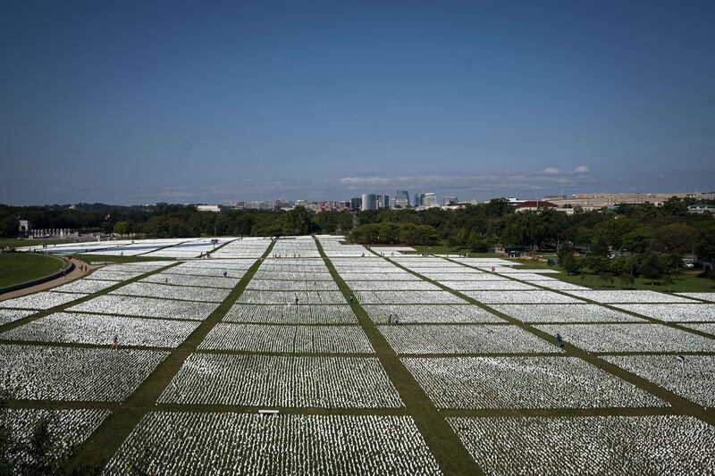 WASHINGTON, DC - SEPTEMBER 19: In this elevated view, people walk through the flags of the 'In America: Remember' public art installation near the Washington Monument on September 19, 2021 in Washington, DC.  The installation commemorates all the Americans who have died due to COVID-19.  It's based on a concept by artist Suzanne Brennan Firstenberg, and includes more than 650,000 small plastic flags, some with personal messages to those who have died, planted in 20 acres of the National Mall.    Al Drago / Getty Images / AFP
