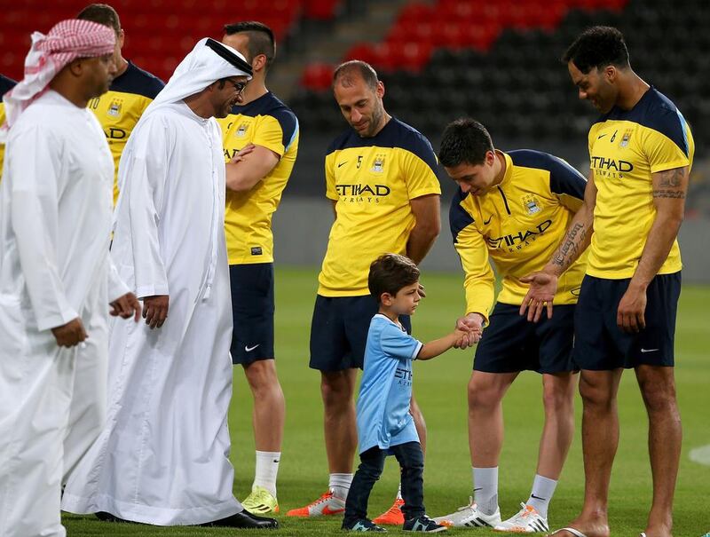 The Manchester City owner Sheikh Mansour bin Zayed’s son shakes hands with the French midfielder Samir Nasri before a team training session on May 14, 2014 at Al Jazira club’s Mohammed bin Zayed Stadium in Abu Dhabi. City play Al Ain in a friendly on May 15. Marwan Naamani / AFP