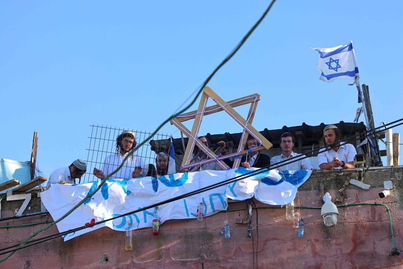 Israeli settlers sit on the rooftop of a house decorated with the Star of David in the Sheikh Jarrah neighbourhood of east Jerusalem on May 15, 2021.  / AFP / EMMANUEL DUNAND
