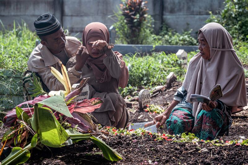 L-R: Mochamad Munif, Ismiatul Urmila, and Munidah, the father, sister and grandmother of Lutvia Damayanti, one of the 131 people killed in the October 1 Kanjuruhan football stadium disaster, mourn over her grave in Malang.  AFP