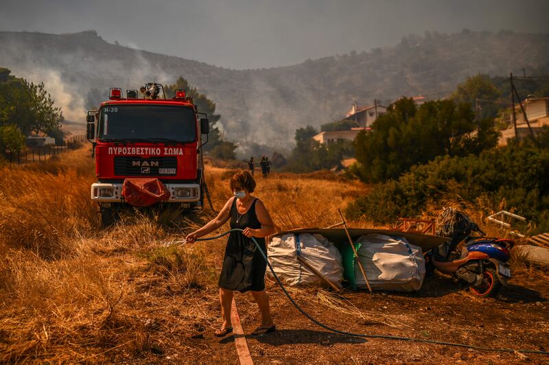 A woman uses a water hose to extinguish a fire in Markati. Three villages south-east of Athens were evacuated as a precaution.