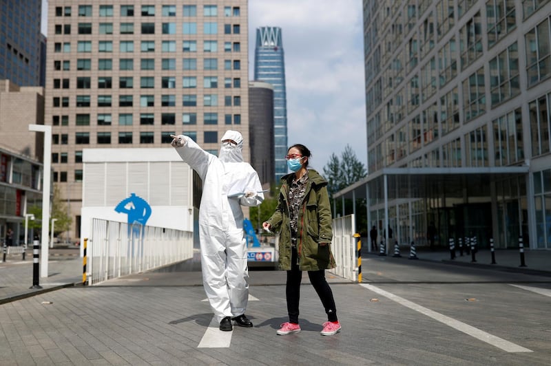 A security guard in Personal Protective Equipment suit gives directions to a passerby during lunch hour in Beijing's Central Business District. Reuters