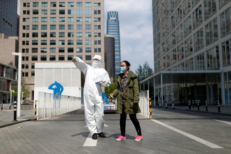 A security guard in Personal Protective Equipment suit gives directions to a passerby during lunch hour in Beijing's Central Business District. Reuters