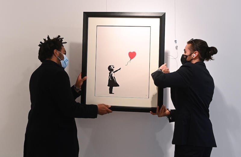 epa09152364 Gallery workers adjust an artwork by British artist, Banksy 'Girl with a baloon' at the 'Millennials' exhibition at the Hofa gallery in London London, Britain, 22 April 2021. The new exhibition features artists such as Banksy, Nina Chanel Abney, Jonas Wood, Josh Sperling, Yoshimoto Nara and will open to the public on 23 April.  EPA/FACUNDO ARRIZABALAGA