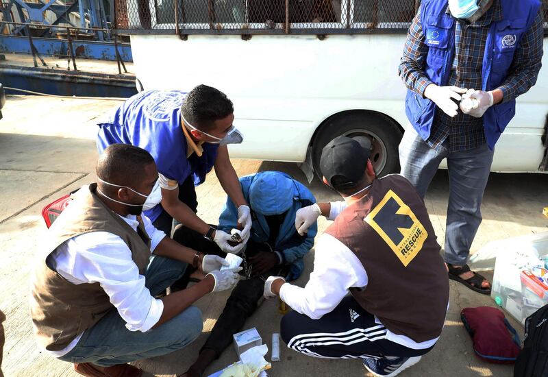 Aid workers tend to a migrant arriving at the naval base in the Libyan capital of Tripoli on April 29, 2021 after the coastguard intercepted an inflatable boat carrying 99 Europe-bound migrants off its west coast.   / AFP / Mahmud Turkia
