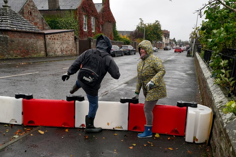Residents climb over a flood defence barrier in the village of Edzell, near Brechin, in Angus, north-east Scotland. PA