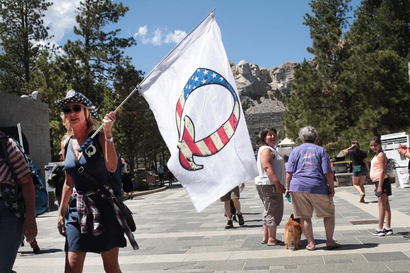 (FILES) In this file photo taken on July 1, 2020 A Donald Trump supporter holding a QAnon flag visits Mount Rushmore National Monument in Keystone, South Dakota. Twitter has removed more than 7,000 accounts linked to the "QAnon" movement over abuse and harassment concerns, saying July 21, it will limit the spread of conspiracy theories by its supporters. / AFP / GETTY IMAGES NORTH AMERICA / SCOTT OLSON

