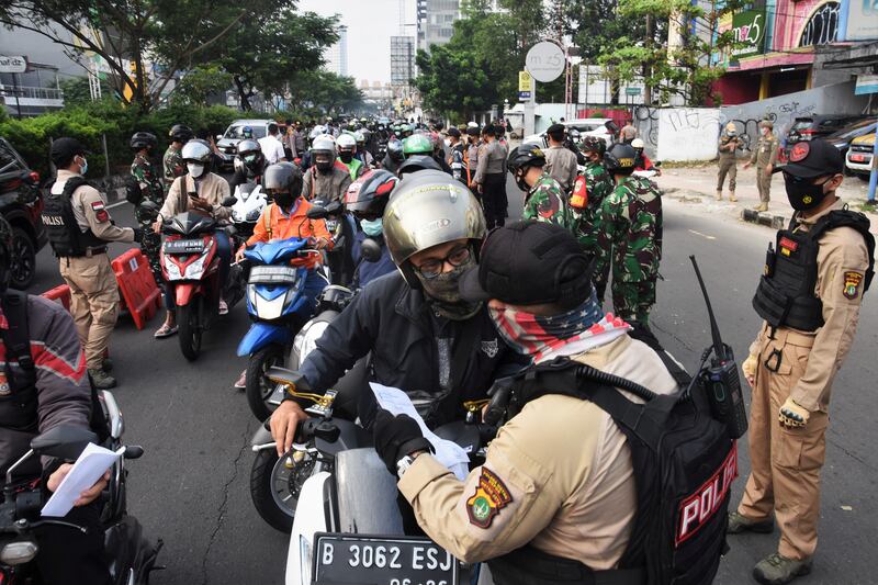 A police officer checks a document from a driver as Indonesia imposes emergency measures, tightening restrictions in Java and Bali amid a surge in coronavirus disease (COVID-19) cases, in Depok, Indonesia.