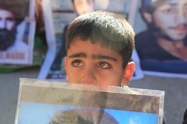 a little kid with tearful eyes is holding the picture of his missing father during the demonstration. Rabia Bugti for The National