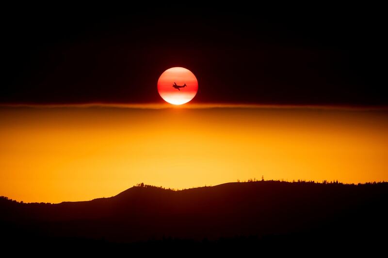 A plane battling a wild fire passes the setting sun near the Yosemite National Park in Mariposa County, California,. Noah Berger / AP Photo