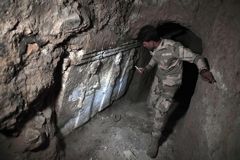 A member of the Iraqi troops stands next to archeological findings inside an underground tunnel in east Mosul on March 6, 2017.  Two winged bulls dating from the Assyrians empire were found in a labyrinth of narrow underground tunnels dug by ISIL in east Mosul. Aris Messinis/AFP